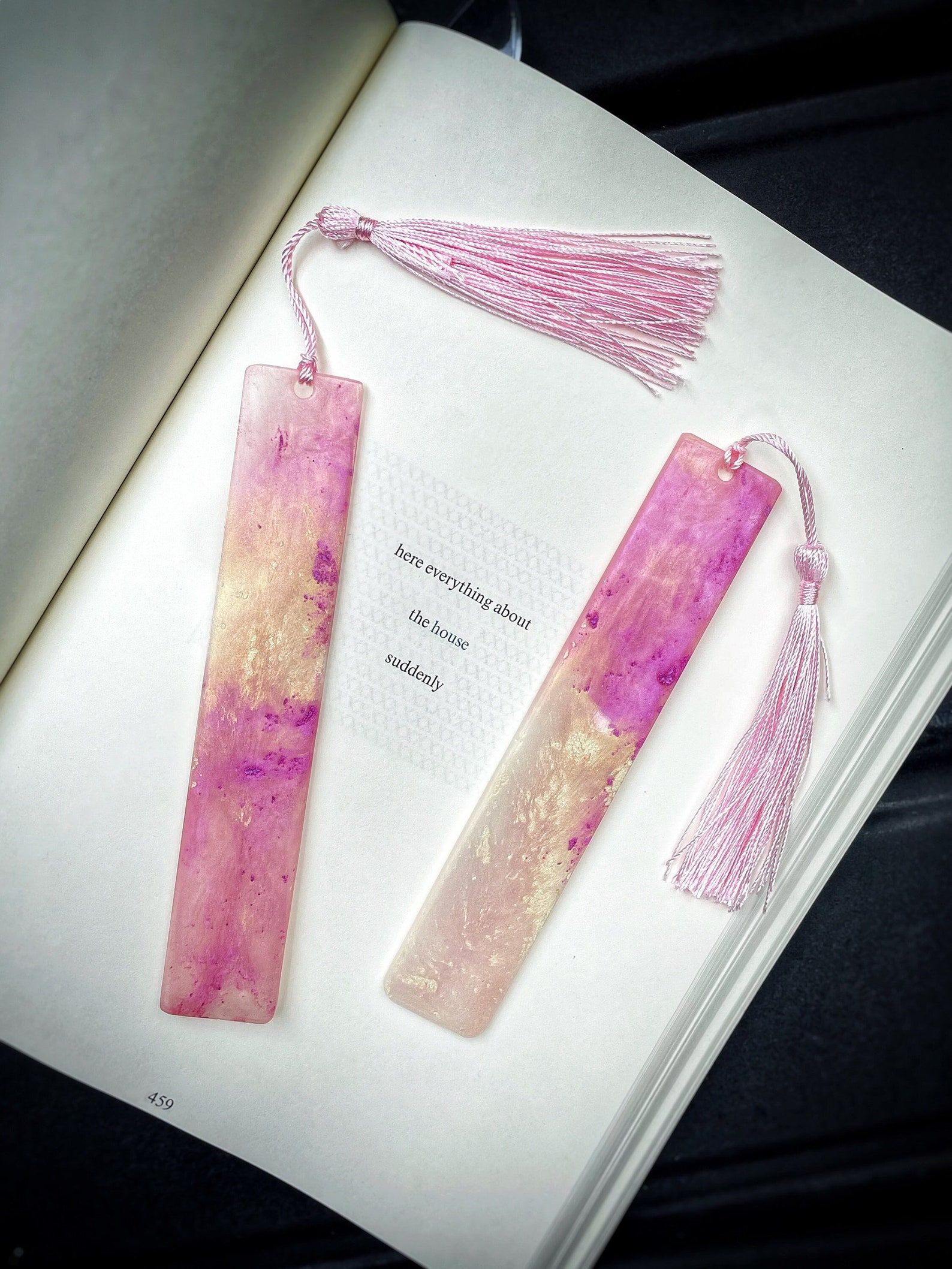 Two pink resin bookmarks on top of an open book. They have long pink tassels. 