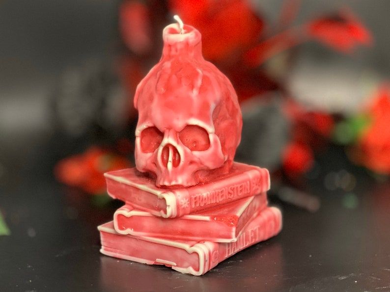 Image of a candle with a book stack and skull on top. It's bright pink. 