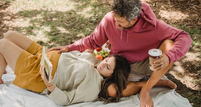 a photo of a couple on a picnic blanket reading. One is pregnant