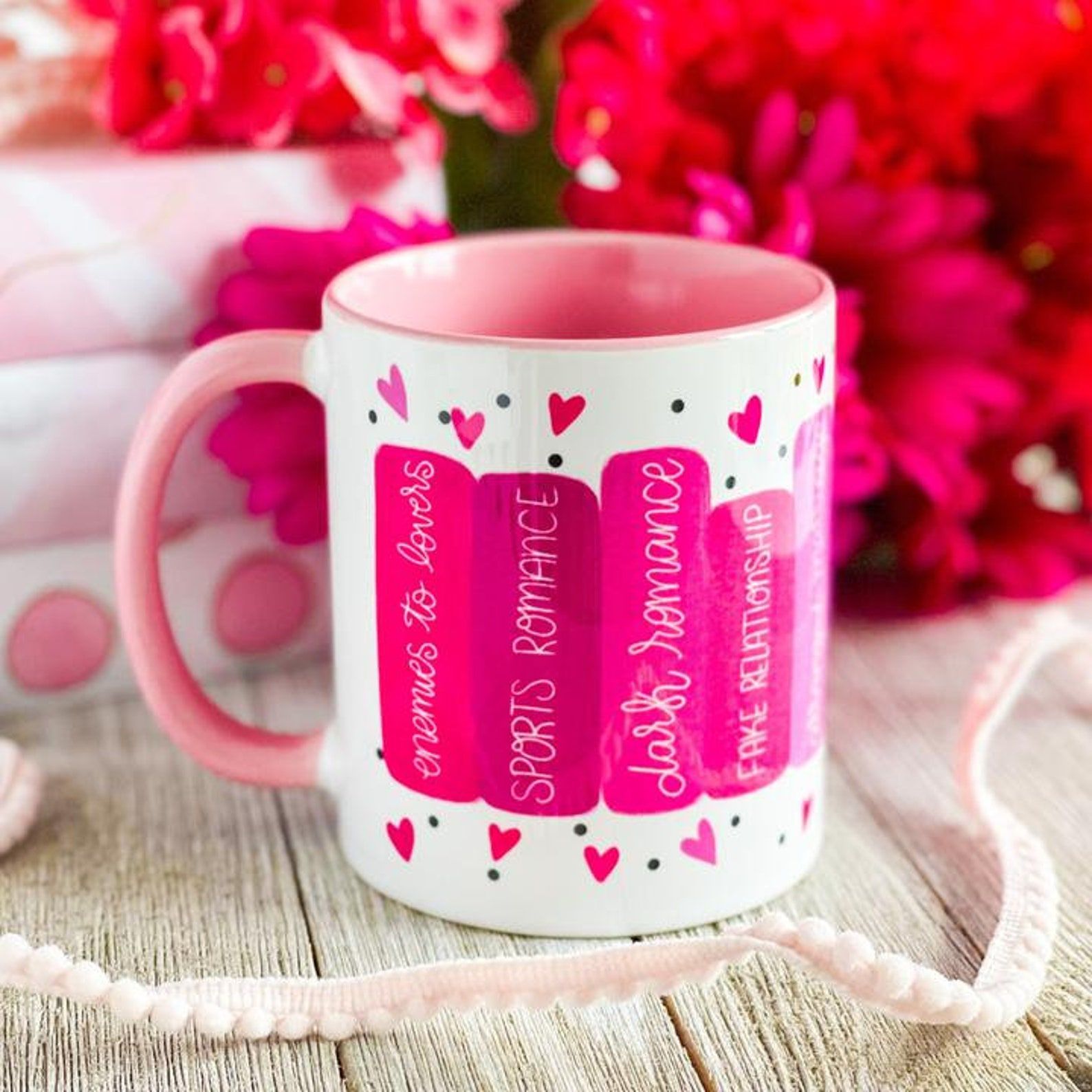 A white and pink mug featuring book spines with various romance tropes.