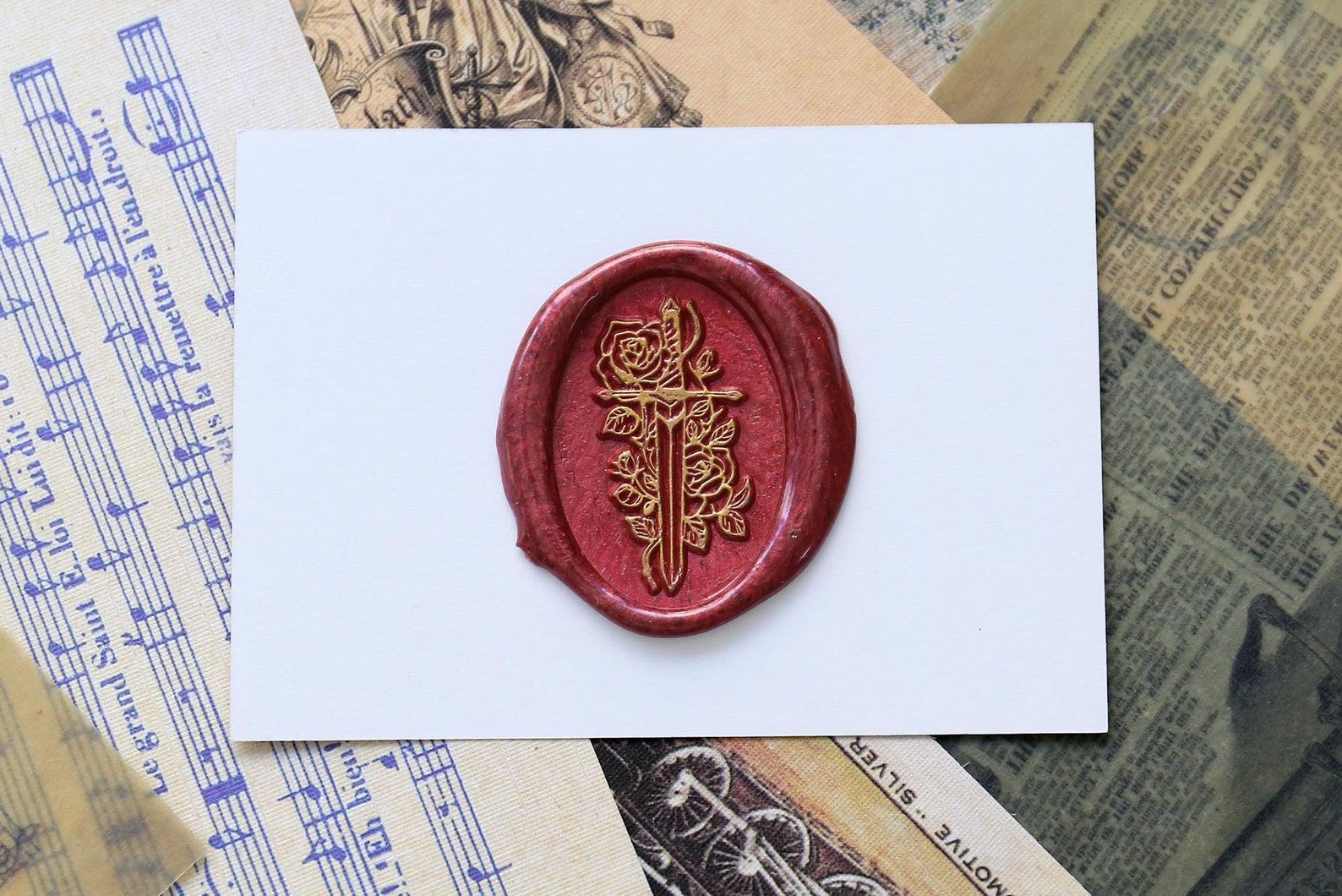 Sceau de cire rouge sur un morceau de papier cartonné blanc.  Le sceau a une épée en or et des roses. 