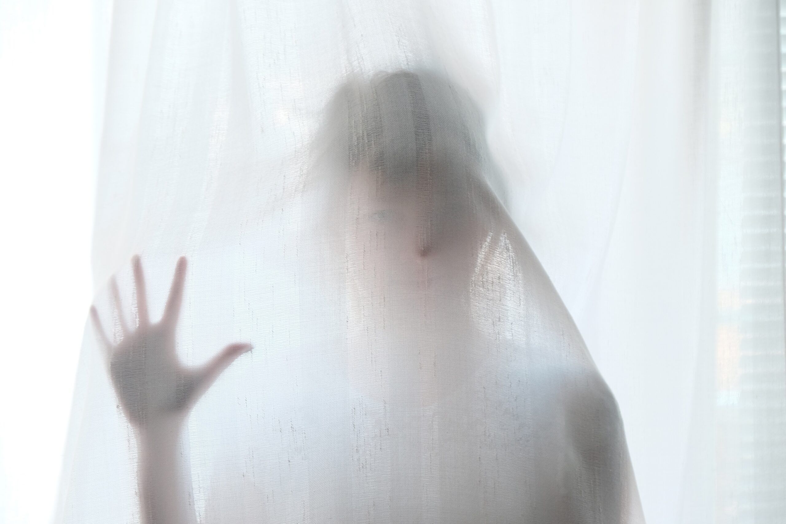 a photo of a woman pressing her face and hand into a sheer white curtain