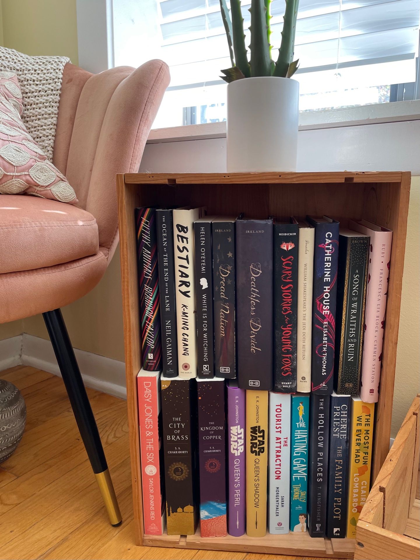 wooden wine crate full of books next to a pink chair