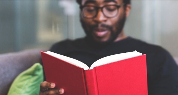 Black man on a couch reading a red book