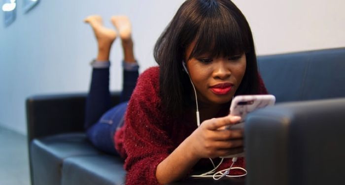 young Black woman listening to something on her phone on couch