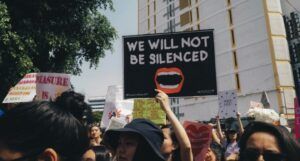 a protest with a person holding a sign that reads we will not be silenced