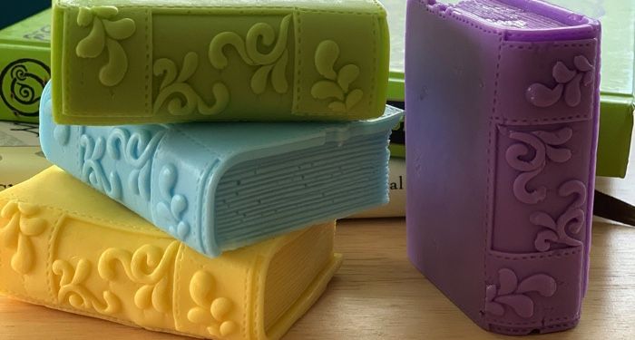 A stack of handmade soaps shaped like books in green, blue, yellow, and purple.