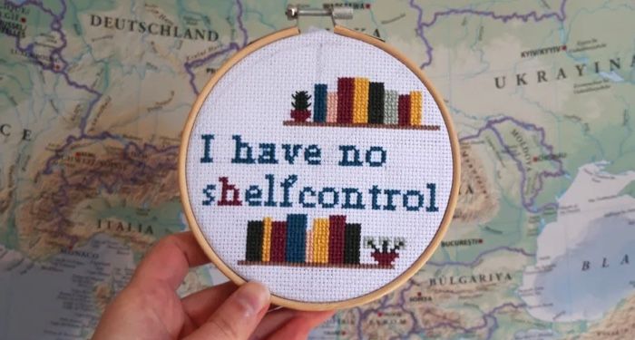 A cross stitch in a hoop that reads "I have no shelf control" and displays two shelves of books
