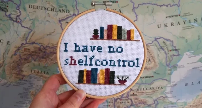 A cross stitch in a hoop that reads "I have no shelf control" and displays two shelves of books