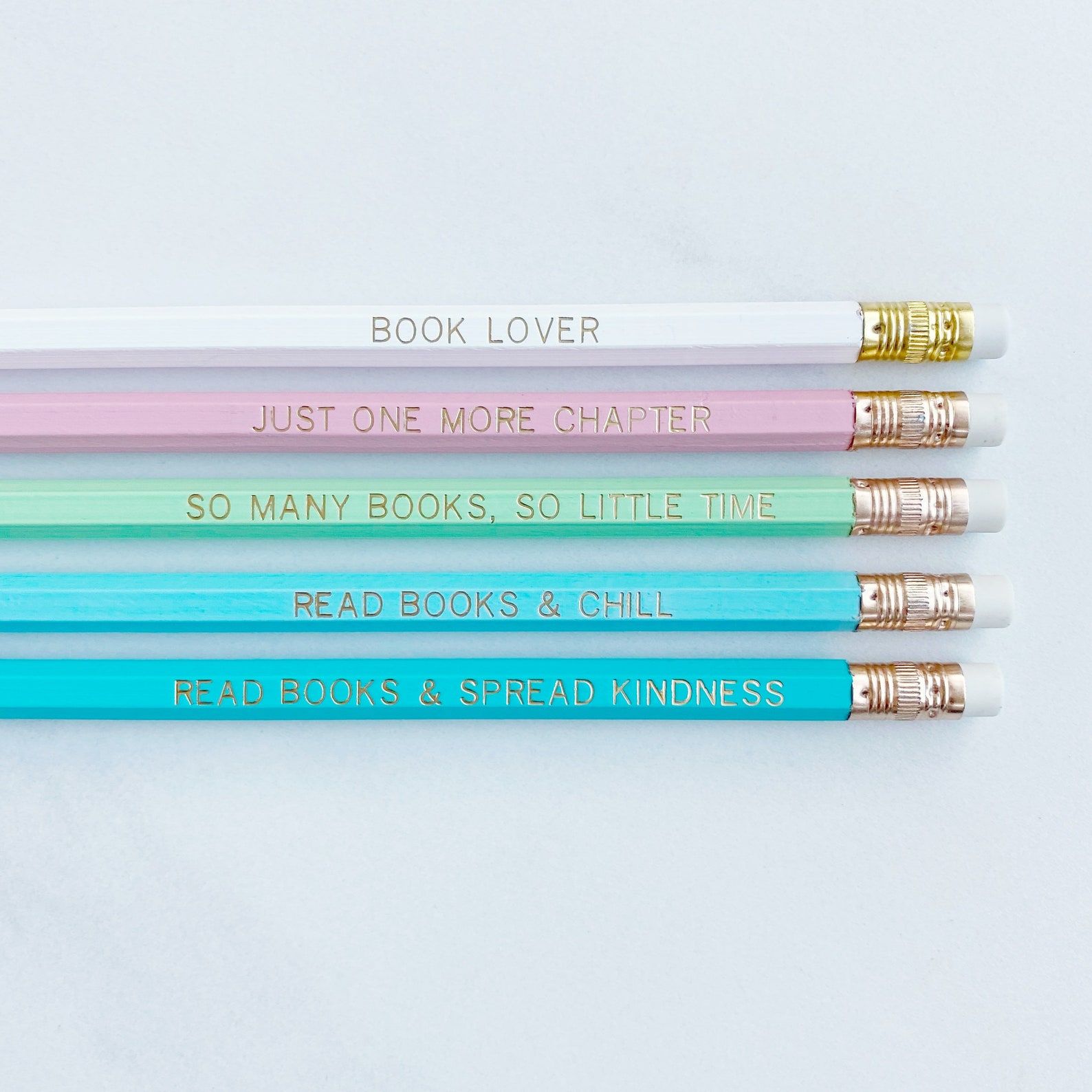 Image de cinq crayons dans diverses nuances de bleu, ainsi que de vert, de rose et de blanc.  Les crayons ont chacun une phrase livresque en texte doré. 