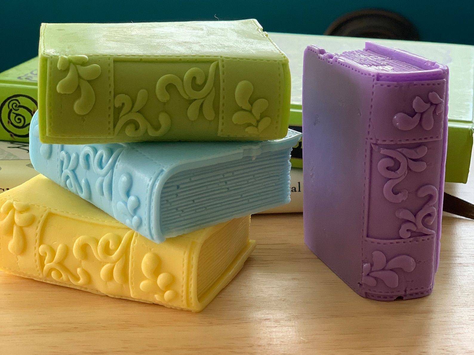 A stack of handmade soaps shaped like books in green, blue, yellow, and purple.