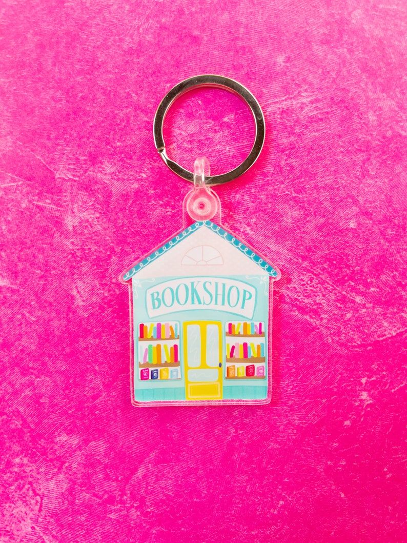 A keychain featuring a cute, blue bookshop. It's on a bright pink background. 