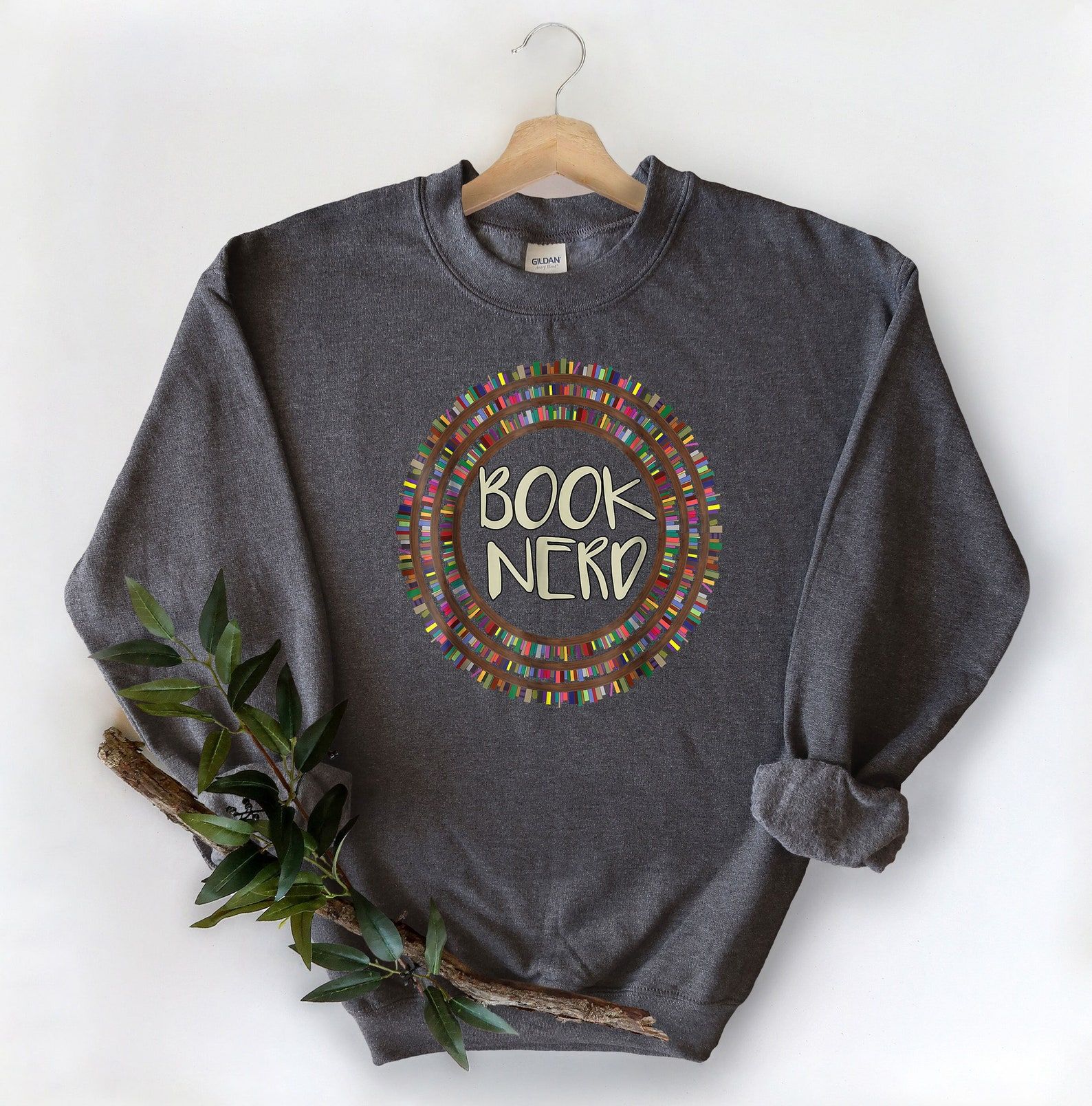 Image of a grey sweatshirt. The center has the words "book nerd" in a cream color. Surrounding the words are three circles made to be bookshelves. 
