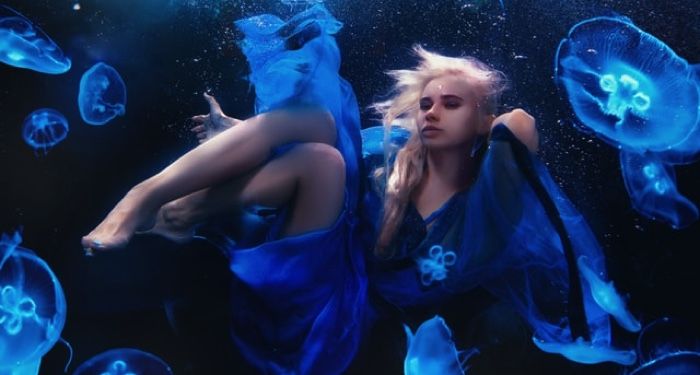 girl floating underwater with blue jellyfish