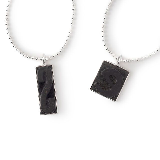 Image of two necklaces each featuring a letter press letter. S and E are shown. 