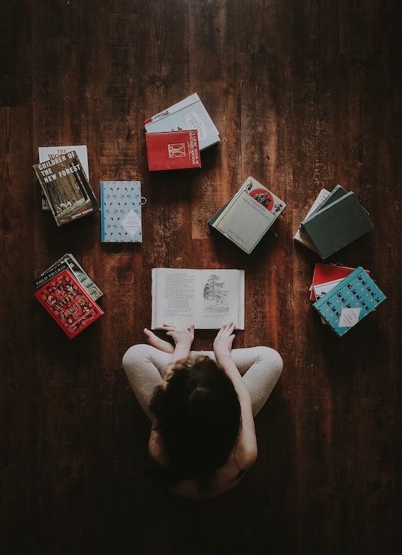 Person reading books on a wooden floor | How to Protect Your Books from Bugs | BookRiot.com