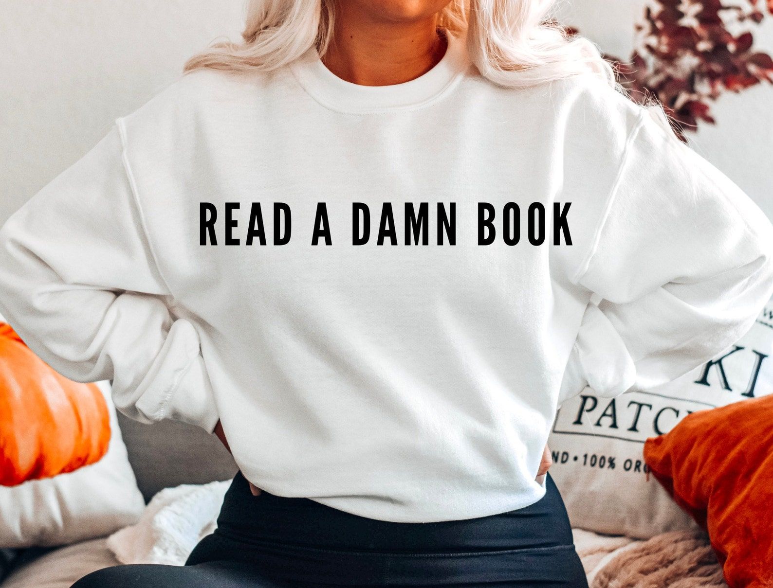 Image of a white sweatshirt with black text that reads "read a damn book." 