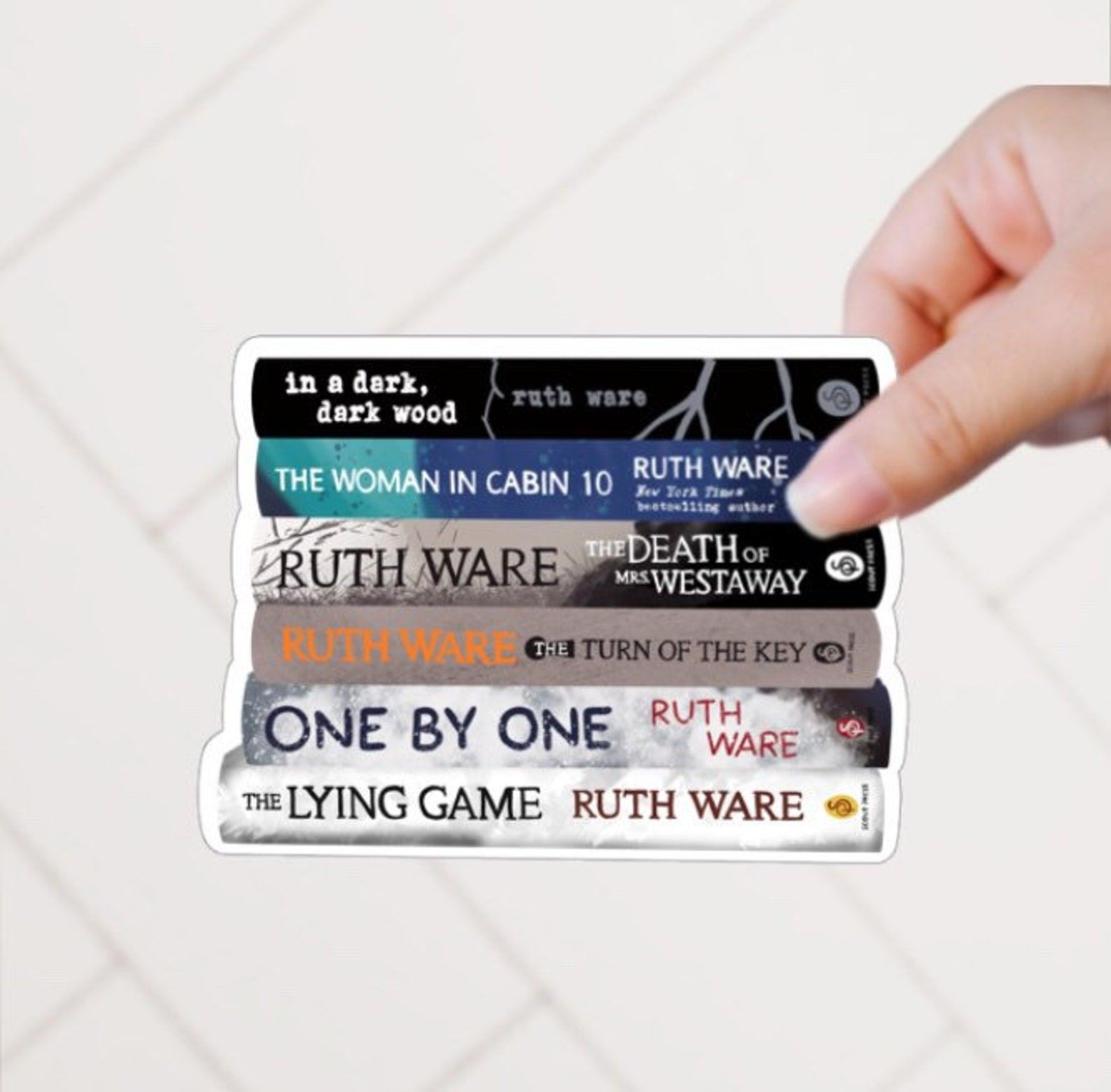 A sticker featuring a stack of Ruth Ware thrillers: In a Dark, Dark Wood; The Woman in Cabin 10; The Death of Mrs. Westaway; The Turn of the Key; One by One; The Lying Game