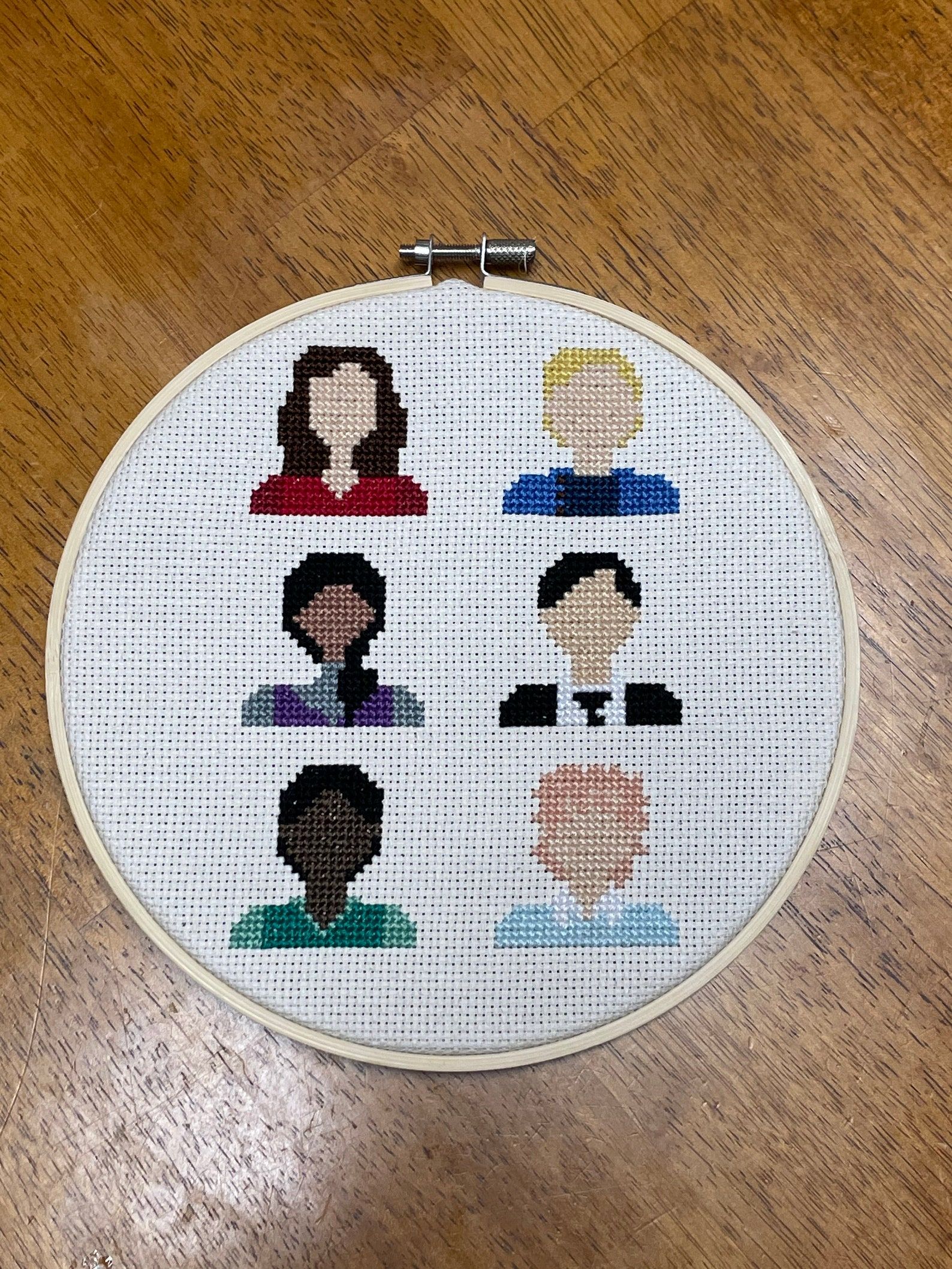 A circular hoop featuring the six protagonists of Six of Crows in cross stitch