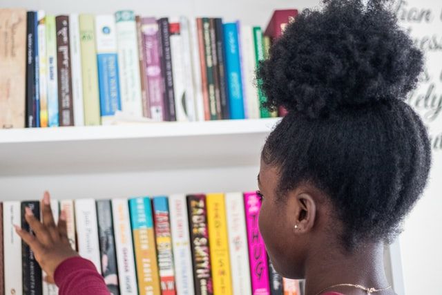 a young Black girl looking for a new book to pick from a bookshelf