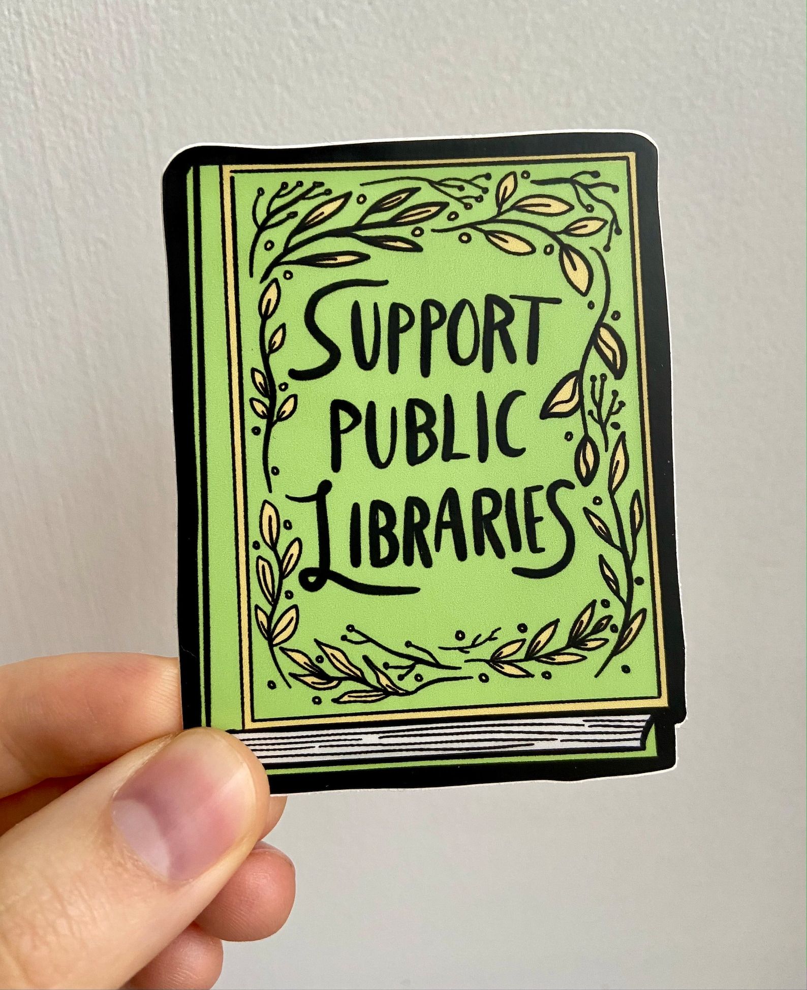 A green book-shaped sticker that reads "Support public libraries"