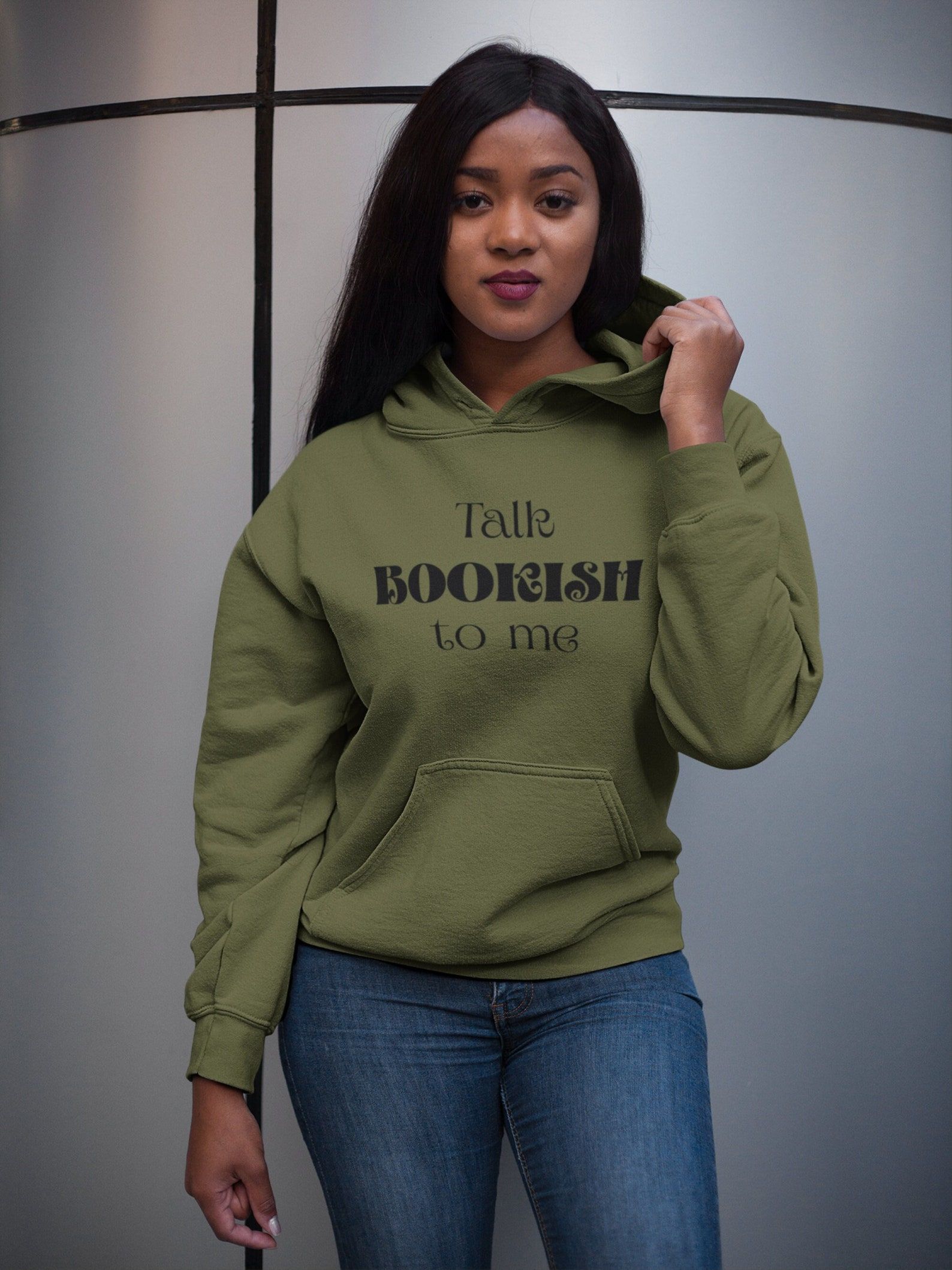 Image of a Black woman wearing an olive green hoodie that reads, in black ink, "Talk bookish to me."
