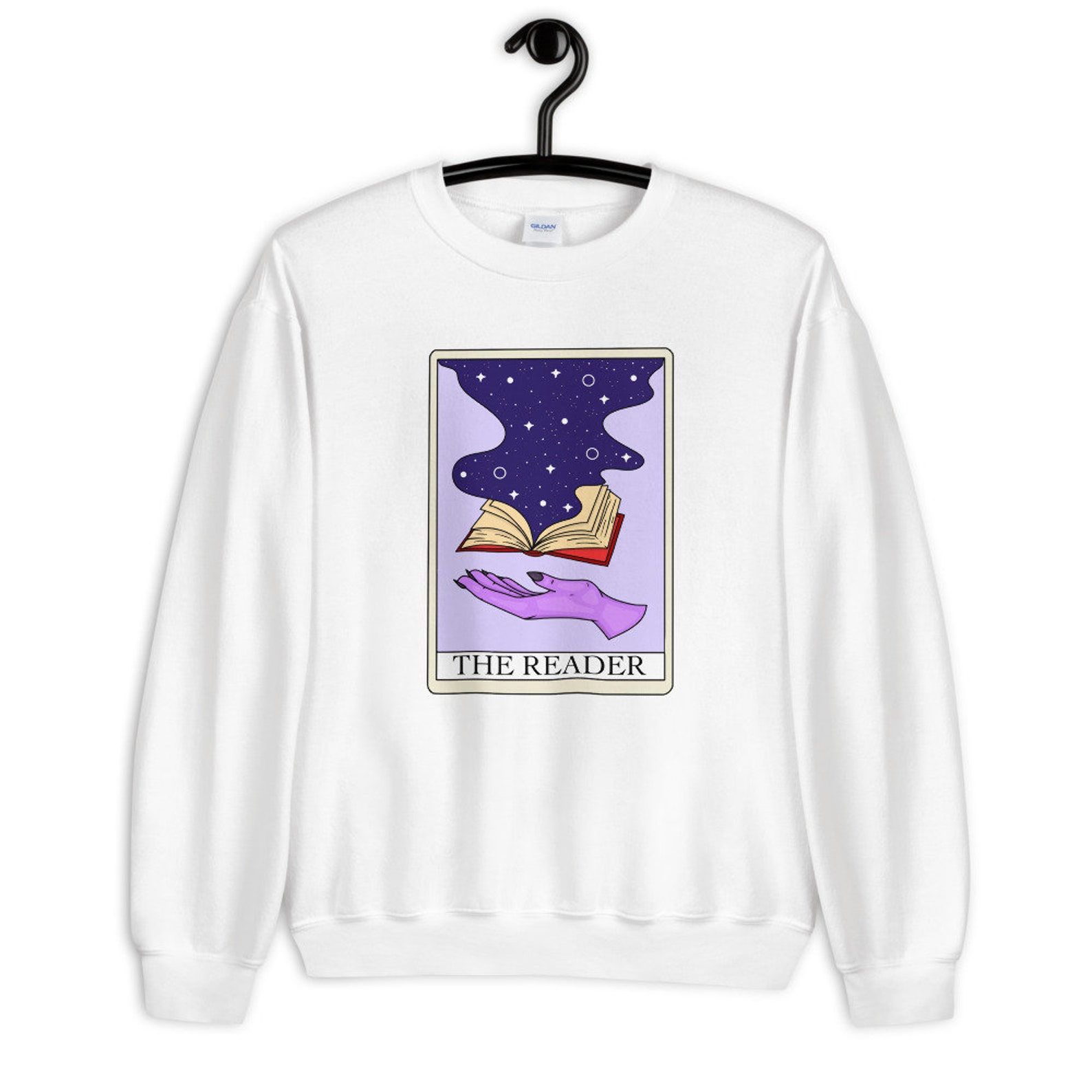 Image of a white sweatshirt with a purple tarot card in the middle. The card features a hand and a book and is titled 