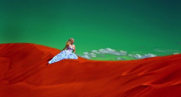 woman sitting on red sand, with a green sky