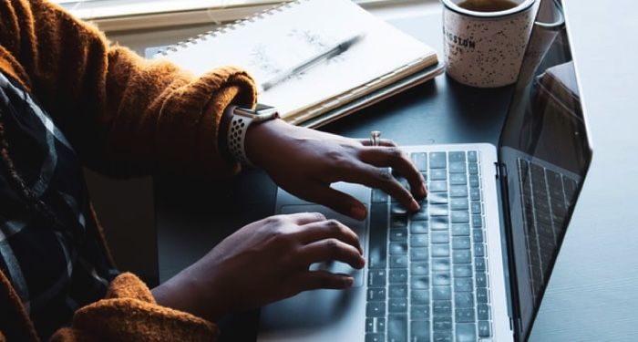 Black woman typing on a computer with cup of tea next to her