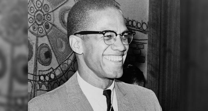 a black and white photo of Malcolm X smiling