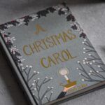 a hardcover copy of A Christmas Carol by Charles Dickens surrounded by star-shaped ornaments and pine cones