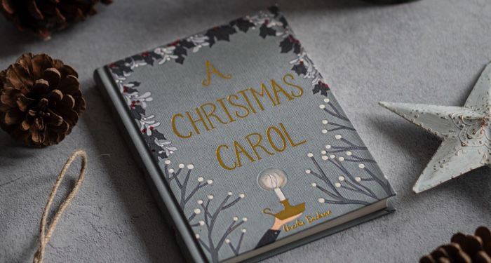 a hardcover copy of A Christmas Carol by Charles Dickens surrounded by star-shaped ornaments and pine cones