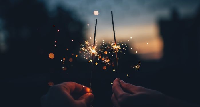 two hands holding up sparklers against a night sky