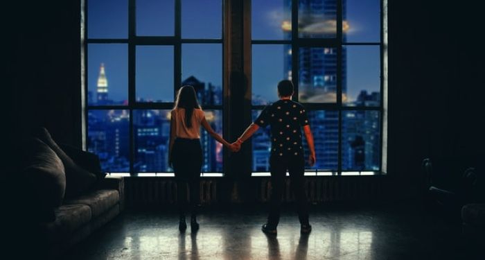 man and woman holding hands in front of a large window in the evening
