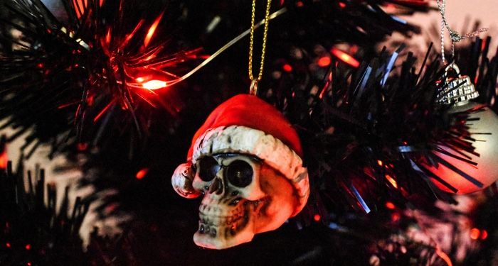 a gold skull ornament hanging a Christmas tree. The skull has a Santa hat on.
