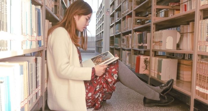 Image of an Asian woman reading on the floor of her library