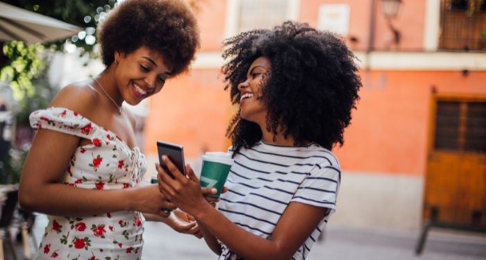 Image of two Black women smiling at a smart phone while outside