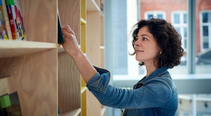 Image of a woman with white skin and dark curly hair at a book shelf in a library