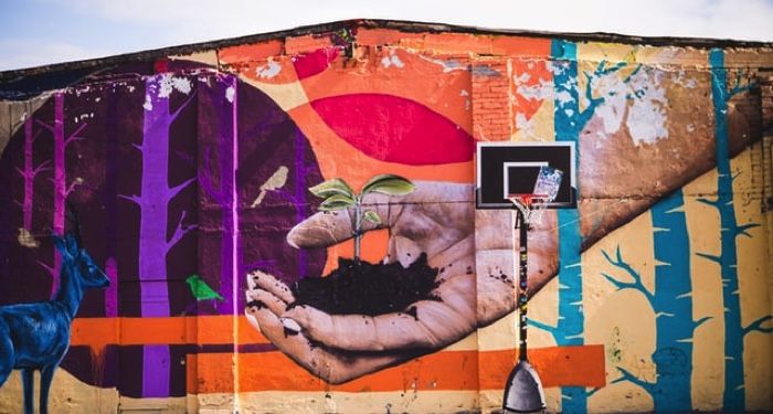 colorful mural showing a hand with soil and a plant sprouting out of it being offered to a smaller blue deer; in front of mural is a basketball hoop