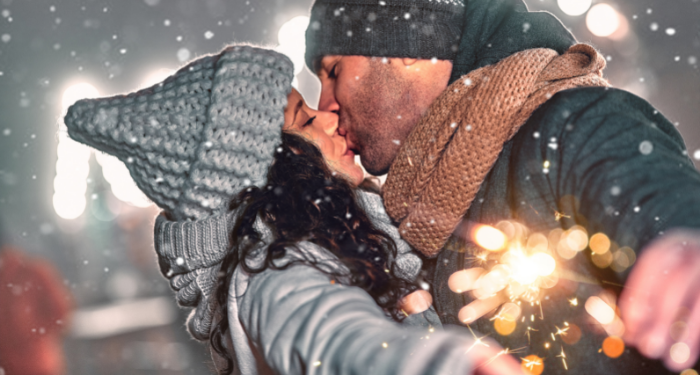 a photo of a white man and woman kissing in the snow while holding a sparkler