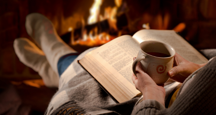 a photo of someone holding a mug and reading in front of a fireplace