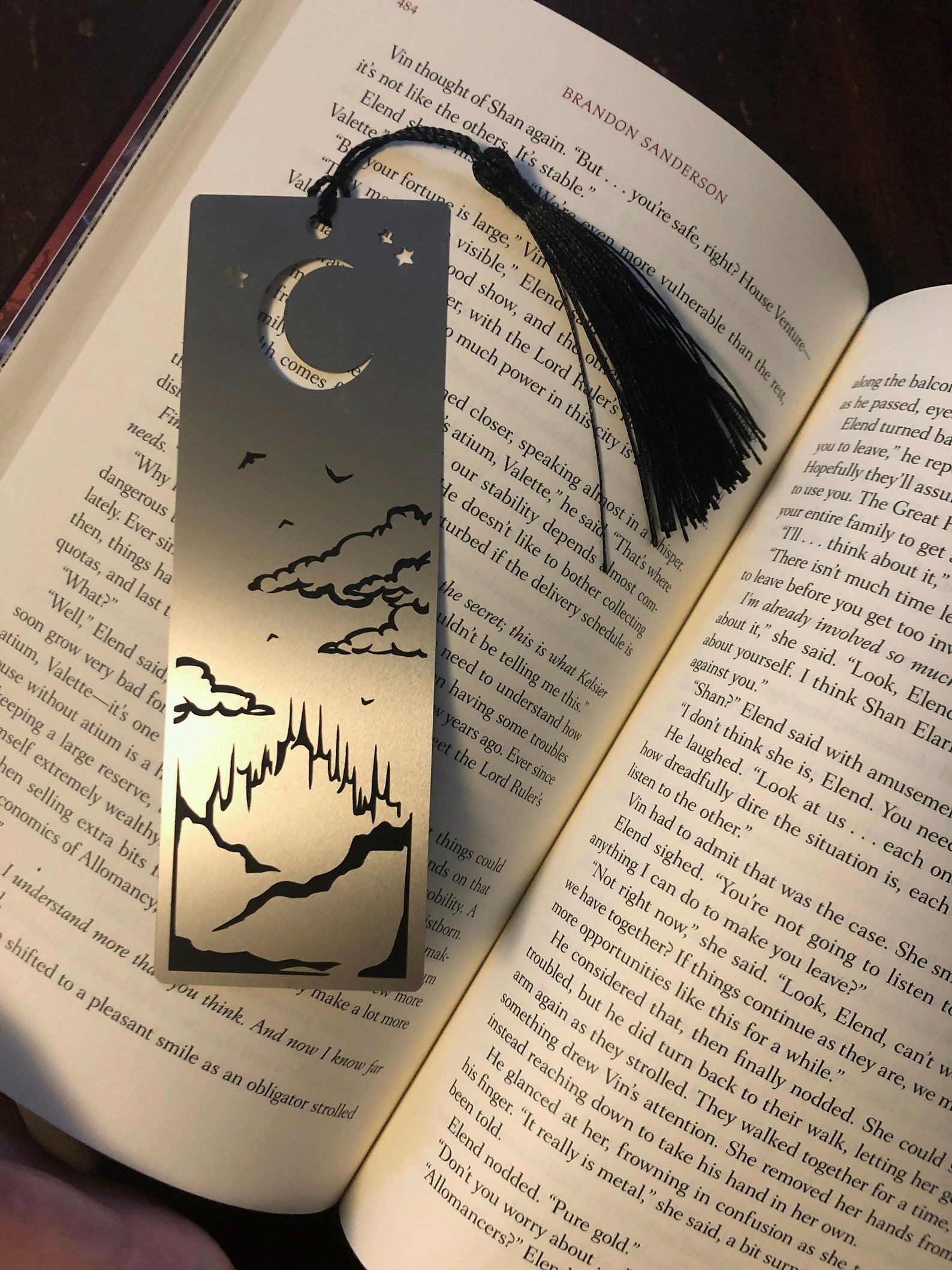 Image of a metal bookmark with a moon and mountains. It's tucked into a book. 