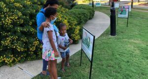 a Black family reads a page from a StoryWalk on a trail