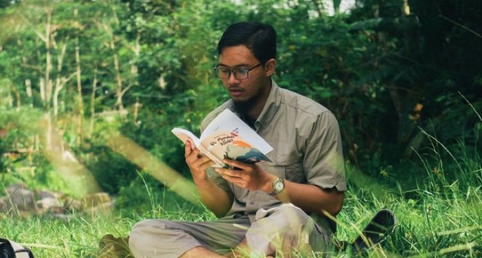 Asian man reading while sitting on grass