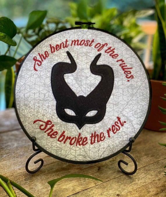 Shades of Magic gift embroidery featuring Lila's mask and the text "She bent most of the rules. She broke the rest."