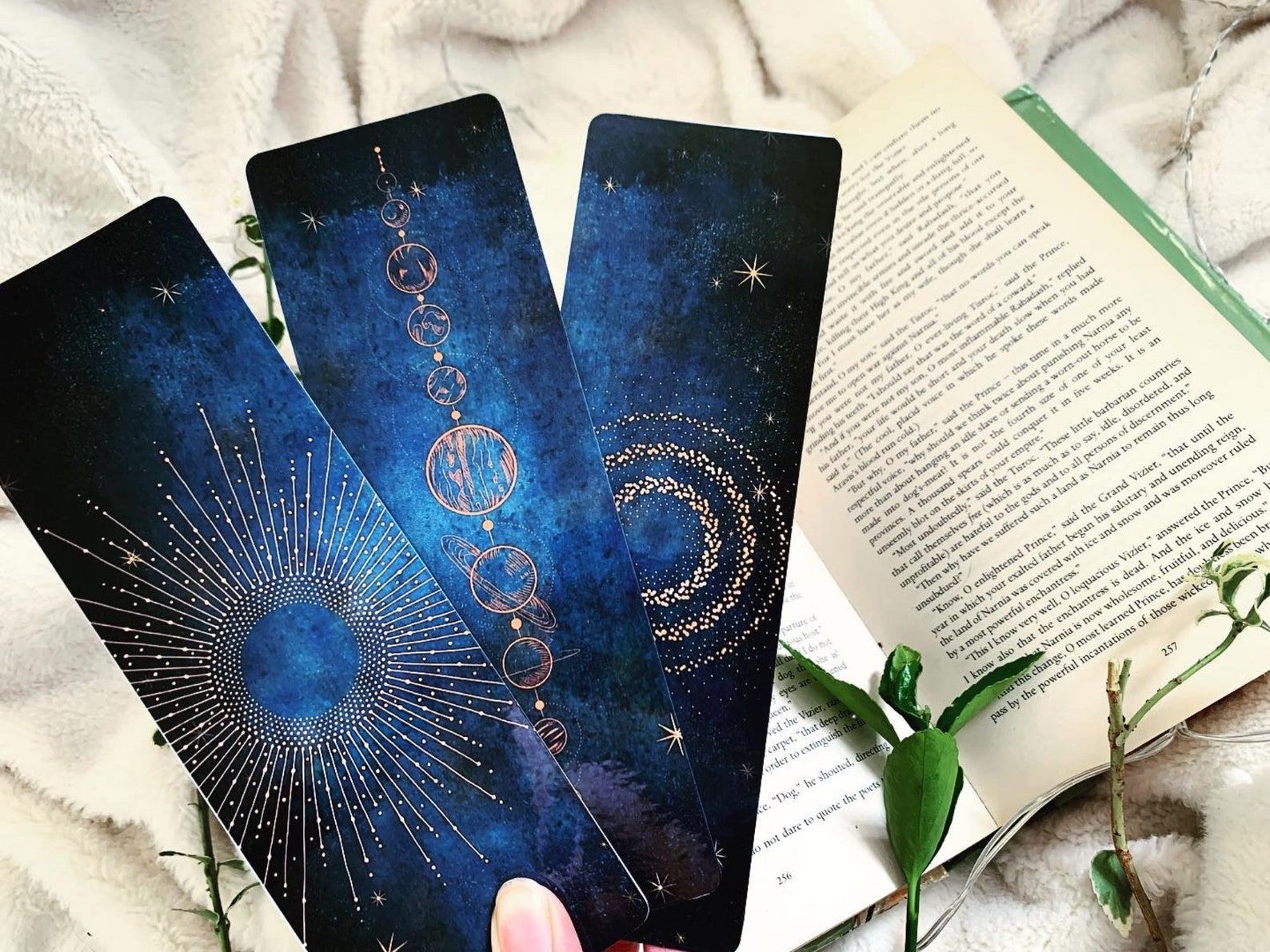 Three deep blue bookmarks. The top features a golden sun. The center has golden moon phases. The bottom has three circles of stars. 