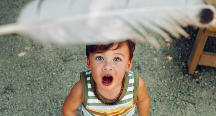 pale skinned little kid looking up at a white feather