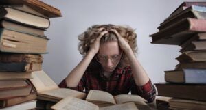 a person reading with stacks of books to either side of them. Person has hands in their hair and appears overwhelmed
