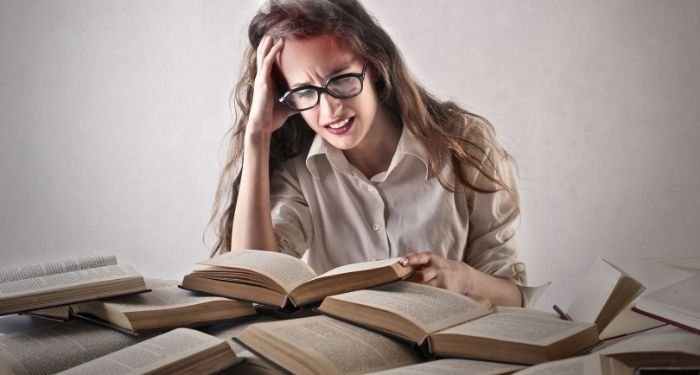 a person with a frustrated expression surrounded by a pile of open books