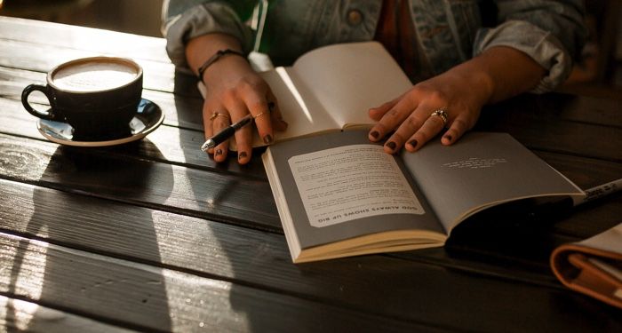 a person holding an one notebook and an open book on a wooden table